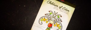 Image: Show logo for Children of Eden. A white posted angled to the right centered on a black background. At the top of the poster, written in black cursive is "Children of Eden" Below the text is a hand drawn apple tree.