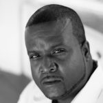 Black and white headshot for Rodney Johnson. Black male with very short brown hair.