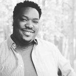 Black and white headshot for Darrell Grant. Black male with short curly black hair and a mustache.